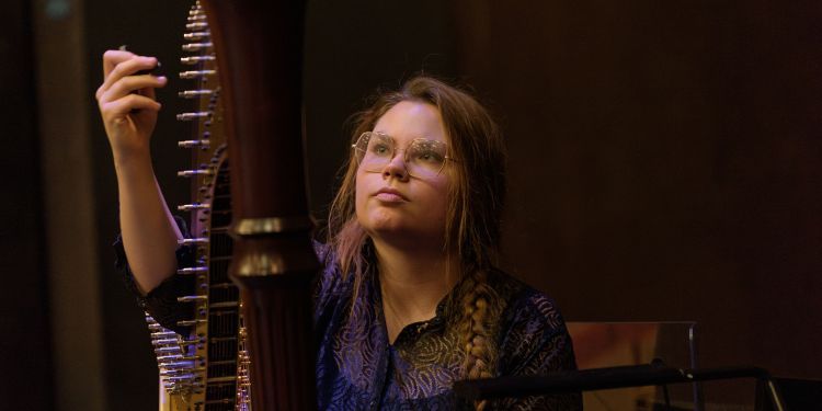 Harpist looking up at their harp with one hand raised