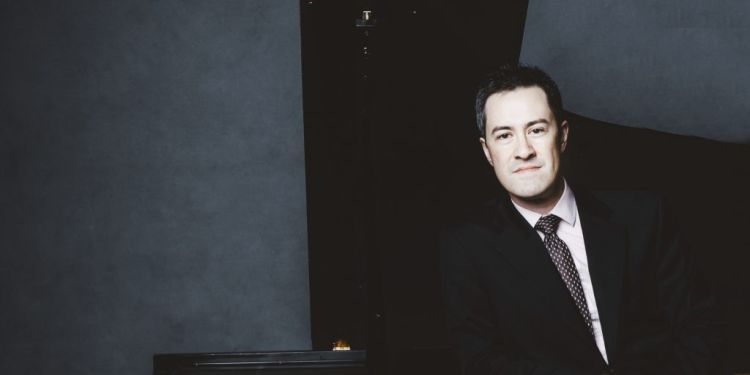 Photo of Andrew Brownell standing next to a piano