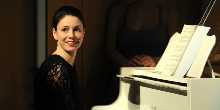 Camille Lemonnier smiling sat at a white piano