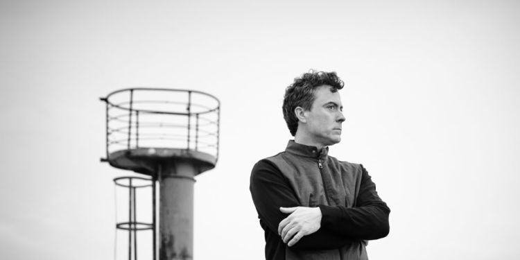 Black and white shot of Paul Lewis standing with a tower behind