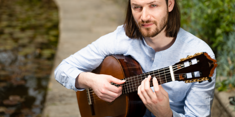 Classical guitar player sat by a pond