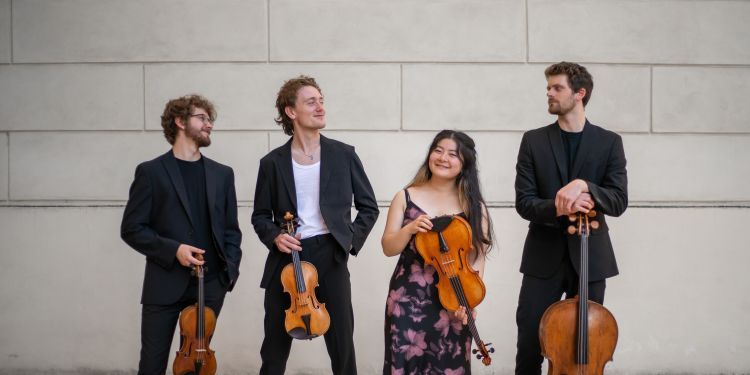 Elmore String Quartet holding their instruments in a line in front of a white brick wall