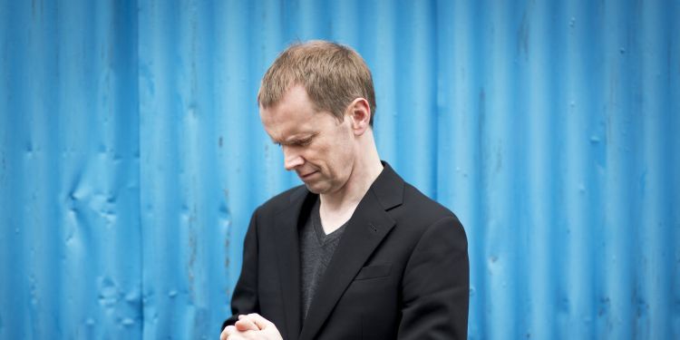 Steven Osborne clasping hands together in front of blue background
