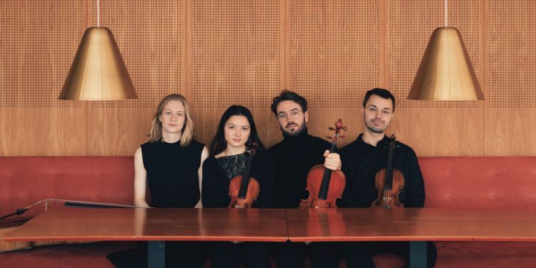 NOVO String Quartet sitting at an empty table, three musicians are holding violins or violas