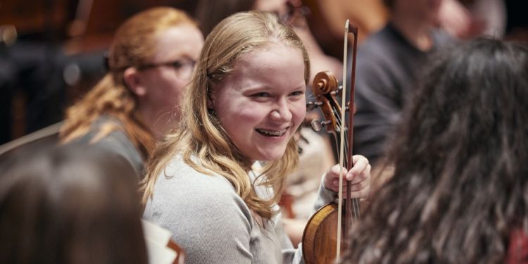 Junior Guildhall student laughing on stage holding her violin 