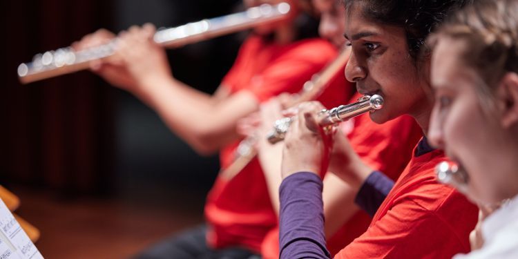 Four students play flutes in a line