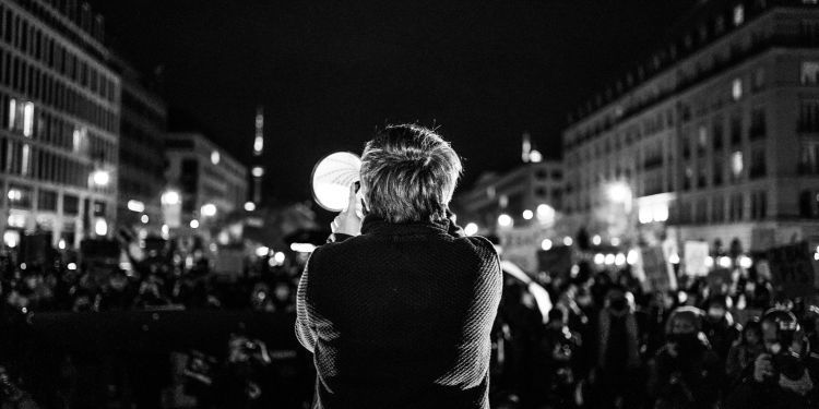 Black and white image of the back of a speaker talking to a crowd through a megaphone