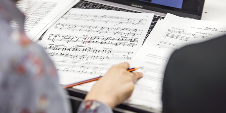 A person notating sheets of music spread out across their desk