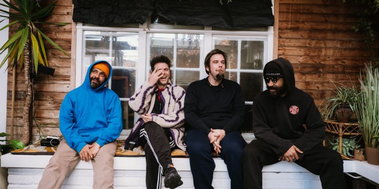 Four artists sat on a wall with flowers and foliage in the background