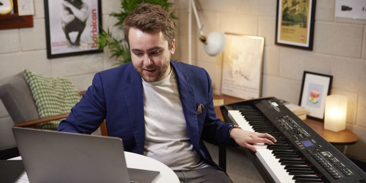Student playing the piano and teaching a student via a laptop online
