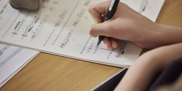 person holding a pen and writing on music theory paper
