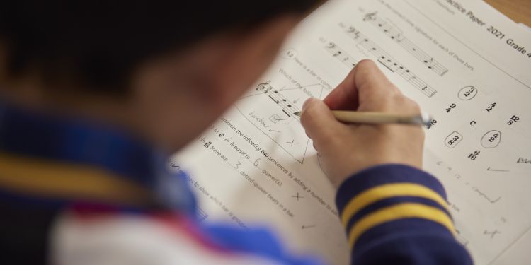 Back of a person holding a pencil and writing on music theory exam paper