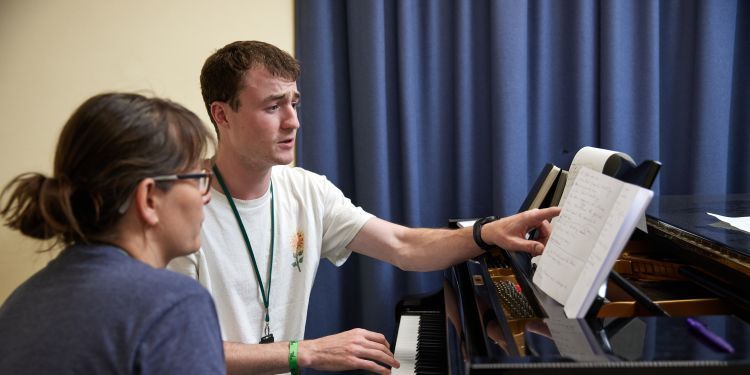 Two course participants sit at a piano writing music together