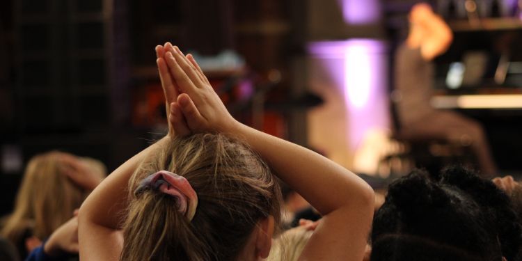 A student in a concert venue holds their hands over their head