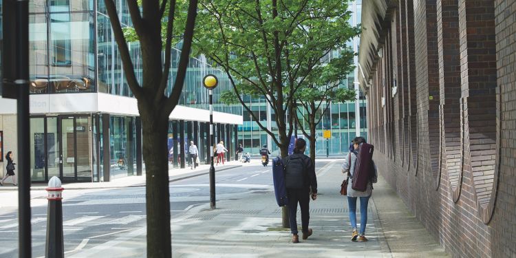 Musicians with instrument cases walking down street outside Milton Court