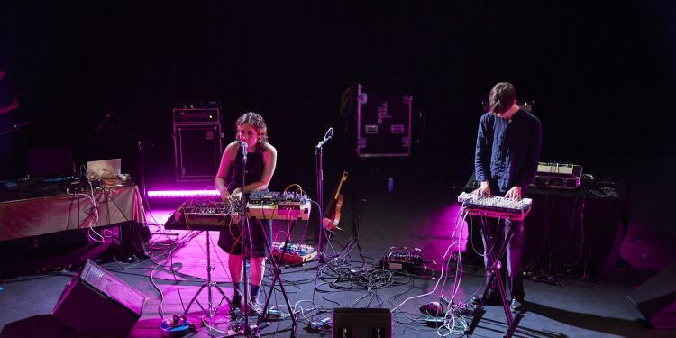 Two students on stage standing and playing a keyboard and sample pads with one student playing and also singing into a microphone