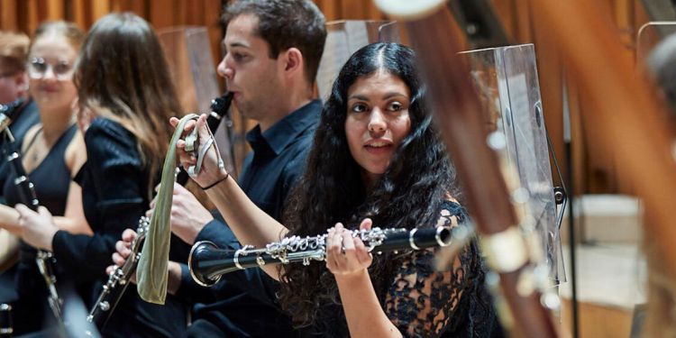 Students on stage holding wind instruments as part of the orchestra