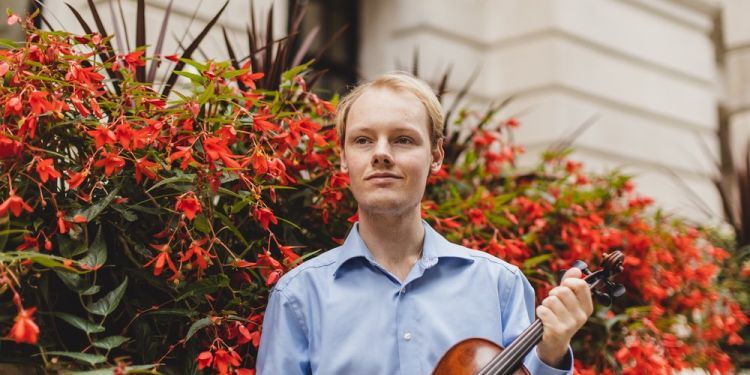 Kryštof Kohout holding violin in front of red flowers