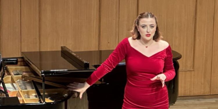 Vocal singer wearing red dress standing with their hand on the piano with a pianist playing