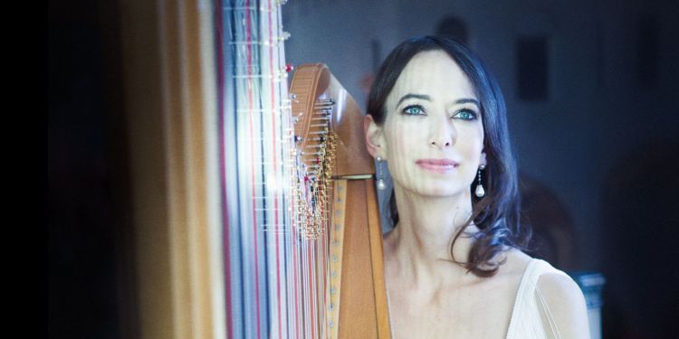 Gwyneth Wentink sat holding a harp wearing a white v-neck dress