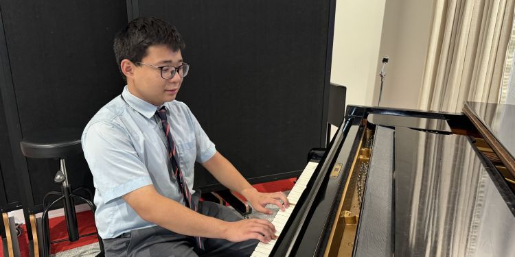 A young musician wearing a blue shirt and tie sits at a piano playing music.