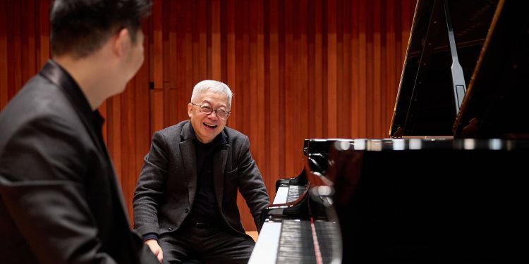 Gabriel Kwok smiling, seated at piano next to Guildhall student