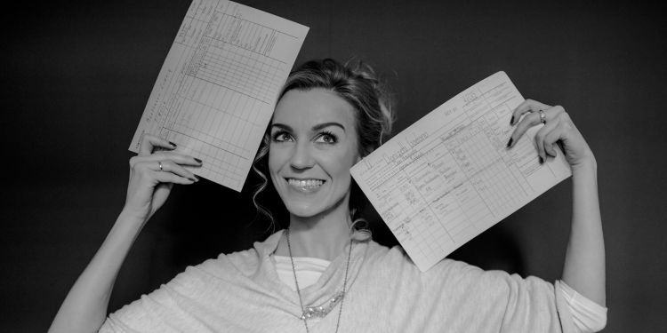 Joanna Freszel smiling holding two sheets of paper in either hand by her face