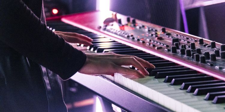 Electronic and Produced Music Students playing the keyboard on stage with a pink hue light in the background