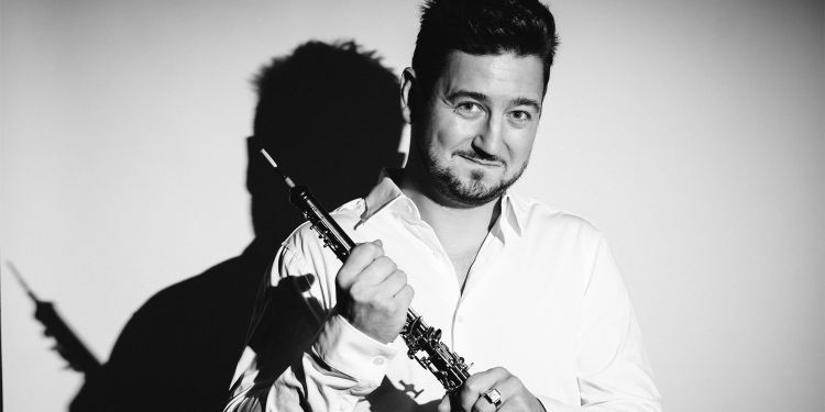 Black and white image of Philippe Tondre holding his oboe smiling whilst wearing a long sleeve white shirt 