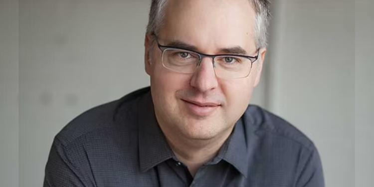 Jimmy Briére wearing a long sleeve blue shirt and a pair of glassses