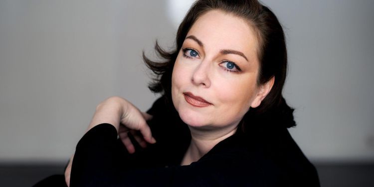 Dorothea Röschmann wearing a long sleeve black top looking at the camera smiling