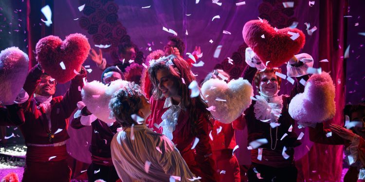 Romantic scene with actors holding pink fluffy hearts and confetti fluttering around the central couple
