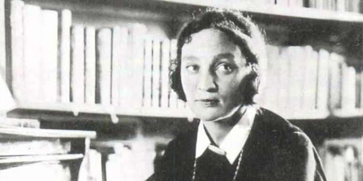 Black and white image of Maria Yudina sat next to a piano