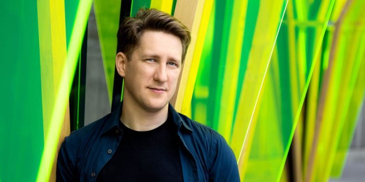 Conductor Joshua Weilerstein standing in front of a vibrant green background
