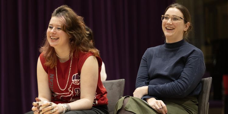 Two people seated in front of a purple curtain, engaged in conversation.