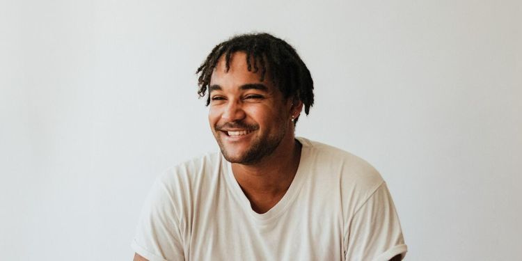 Aaron Azunda Akugbo wearing a white tshirt smiling and looking to the left of the camera