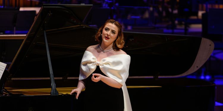 Vocal student wearing a black and white evening dress performing on stage in front of a piano 