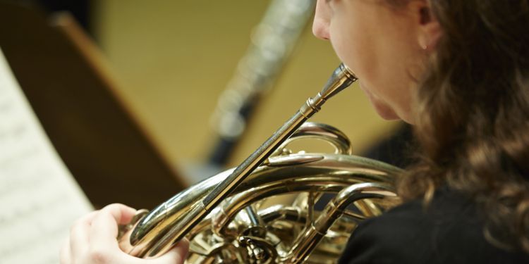 Close up shot of a female presenting student playing the french horn 