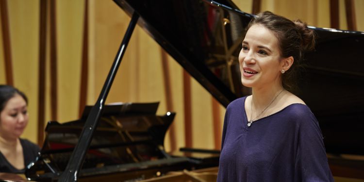Female presenting singer stood next to a pianist 