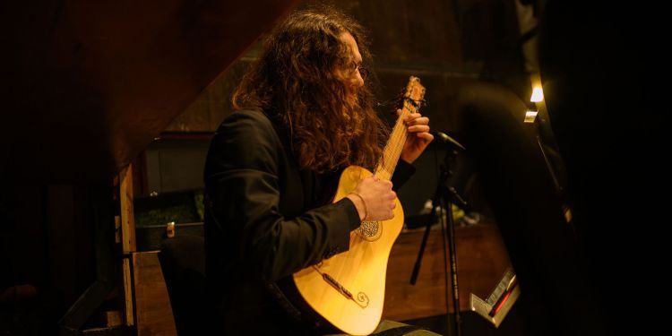 Student on stage playing a Baroque guitar