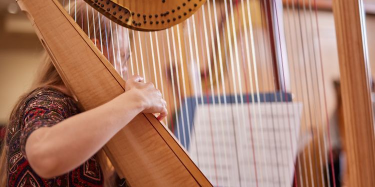 A young girl holds a harp and is reading music 