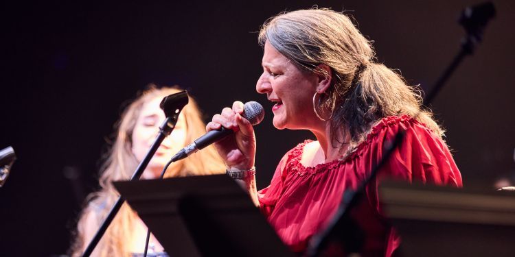 A lady sings into a microphone in front of a music stand