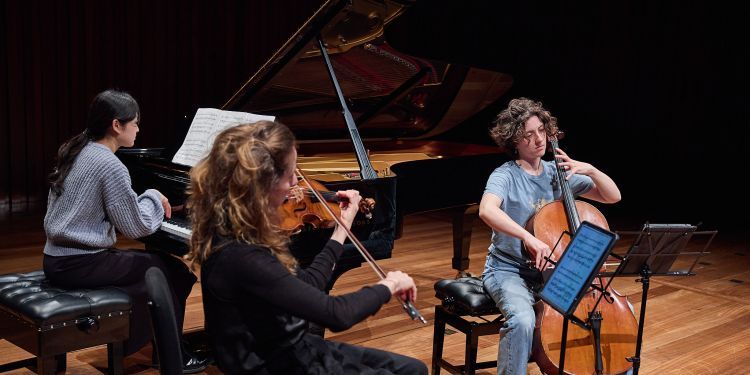 Three students on stage performing, one on piano and two playing strings