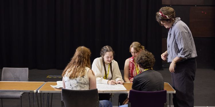 The course tutor stands over a table of four young people working