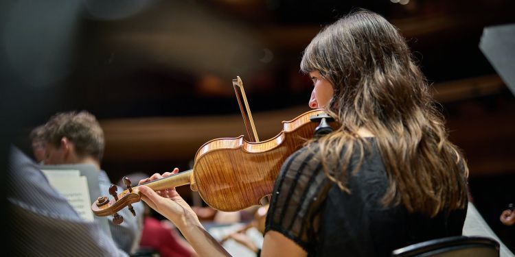 The back of a strings student on stage playing the violin