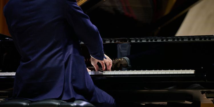 Close up shot of a student wearing a blue suit playing the piano 