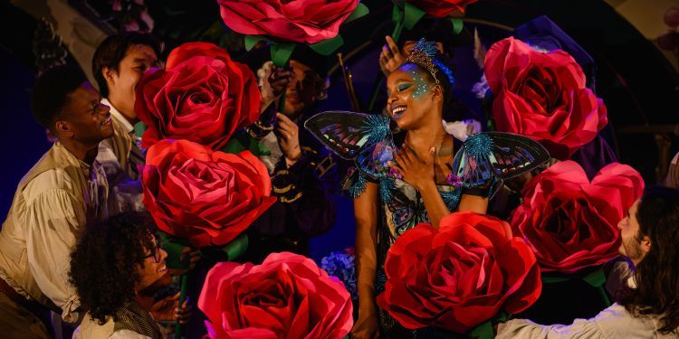 An opera student smiling surrounded by large red roses held in a circle around them 