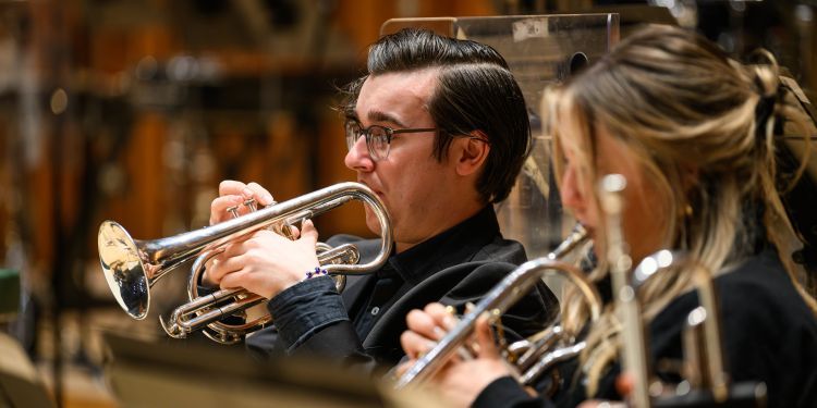 Brass student performing on stage as part of the orchestra