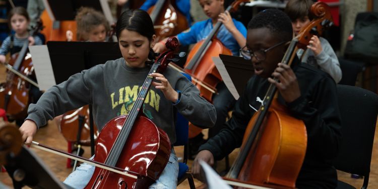 Two cellists play in front of a music stand 