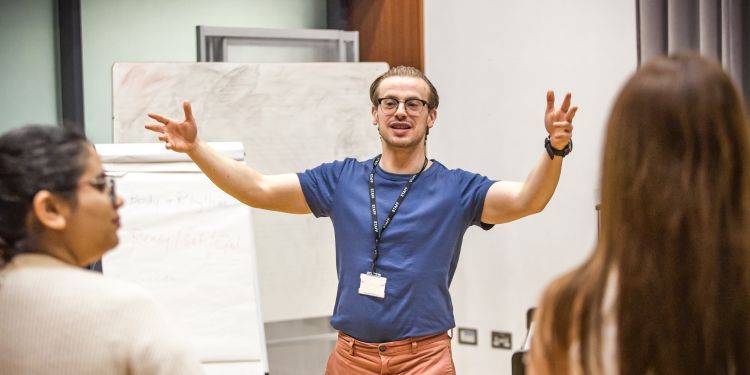 Aled the course tutor is standing in front of the class with his arms animatedly in the air